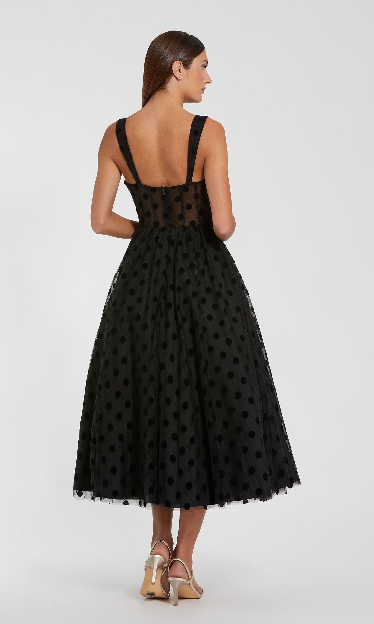 Woman wears the Mac Duggal 27539 Black Midi Polka Dot Party Dress, featuring a sheer back and full tea-length skirt, paired with heels and facing away from the camera.